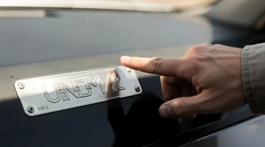 Gros plan sur un numéro VIN gravé sous un pare-brise automobile, éclairé par une lumière naturelle latérale, symbolisant la vérification d'authenticité d'un véhicule d'occasion