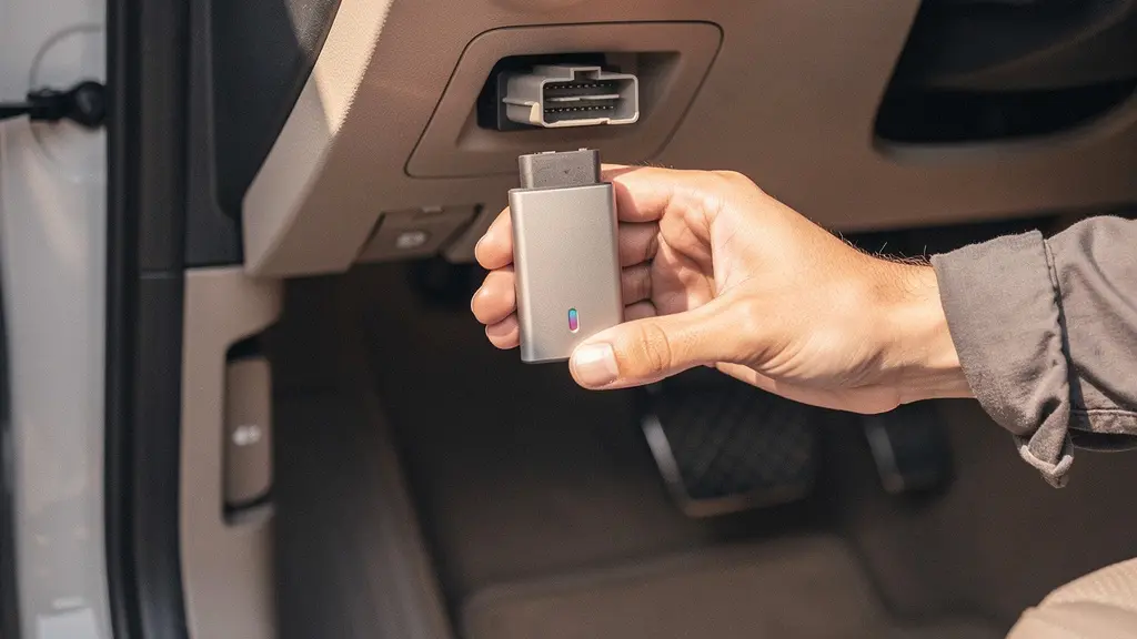 Gros plan sur une main branchant un dongle OBD-II dans la prise diagnostic située sous le tableau de bord d'un véhicule, symbolisant la vérification électronique du kilométrage